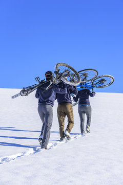 eine Gruppe Radfahrer trägt das Rad im Schnee bergauf