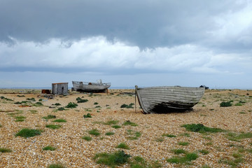 Storm clouds gather over the beach at Dungeness, Kent, with abandoned buildings and boats.