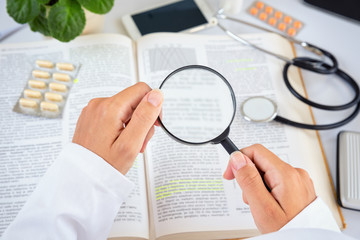 Close up of a female doctor reading professional literature with magnifying glass.