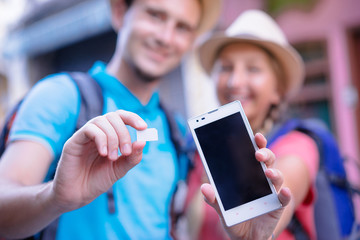 Travel and communication. Young couple of travelers showing sim-card and screen of smartphone....
