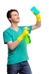 Housekeeping concept. Studio portrait of handsome young man in gloves cleaning glass with wisp and sprayer. Isolated on white.