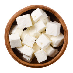 Greek Feta cheese cubes in a wooden bowl on white background. Cubes of a brined curd white cheese made in Greece from milk of sheeps and goats. Crumbly aged cheese with slightly grainy texture. - obrazy, fototapety, plakaty