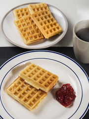 Tasty waffles on a plate with a jam and a cup of tea for breakfast.