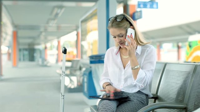 Businesswoman talking on cellphone and browsing internet on tablet on the train station
