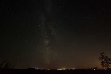 Fototapeta premium Bright stars in the night sky above the city with street lightin