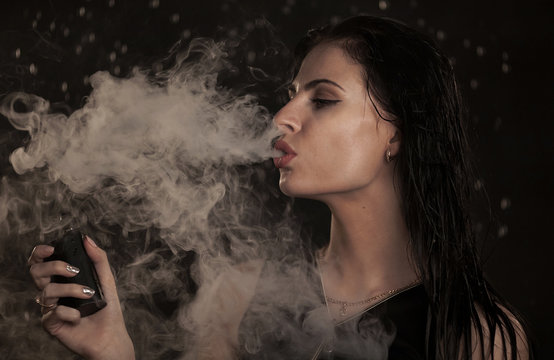 Young beautiful woman vaping e-cigarette. Water flowing on lwoman face.