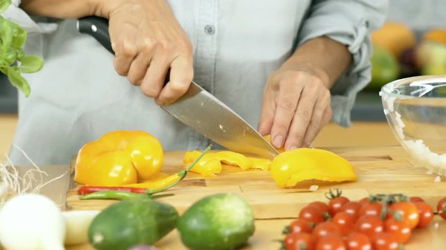 Woman cutting yellow papper on the woode board and throw it into bowl, dolly shot
