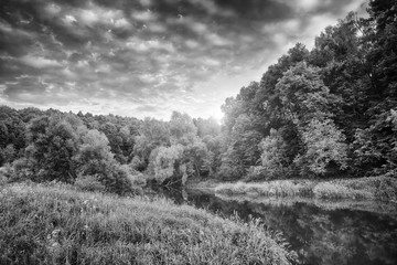black and white spring landscape with a dramatic sky, meadow and river