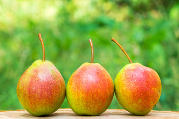 Three ripe organic pears on wooden board, blurred background, selective focus.