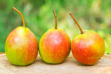 Three ripe organic pears on wooden board, blurred background, selective focus.