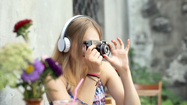 Girl listening music on headphones and doing photos on old, vintage camera
