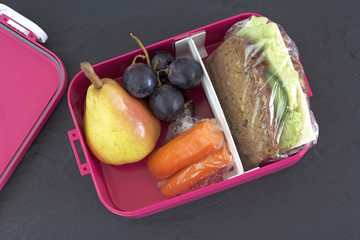Healthy lunch box, cheese sandwich, pear, carrots, and grapes . Topview image.