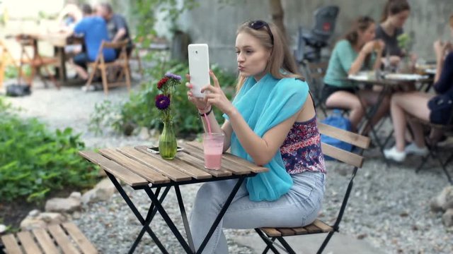 Pretty girl in blue scarf doing selfies on tablet in the outdoor cafe
