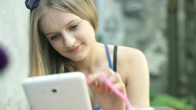 Absorbed girl browsing internet on tablet while sitting in the outdoor cafe
