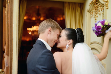 Wedding couple indoors is hugging each other. Beautiful model girl in white dress. Man in suit. Beauty bride with groom. Female and male portrait. Woman with lace veil. Cute lady and handsome guy