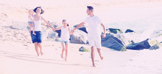 Obraz na płótnie Canvas family of four running on sandy beach on sunny weather