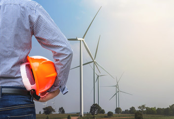 engineer stand holding yellow safety helmet in wind turbines generating electricity power station 
