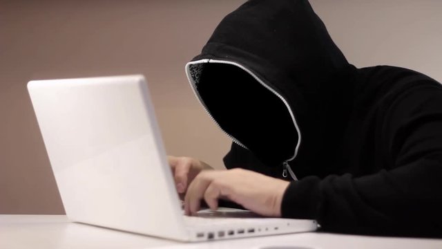 Anonymous hacker in black hood with a laptop