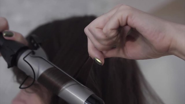 Woman with styling iron doing her curl hair 