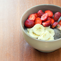Oatmeal breakfast with pieces of bananas,strawberries and bran in bowl with spoon on wood table. Tasty breakfast. Halthy diet