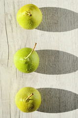 Three juicy green pear with water drops cast a long shadows on  bright wood background 