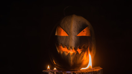 Naklejka premium Scary carved halloween pumpkin in hot burning hell fire flames. The big helloween pumpkin has a mad face with glowing eyes and also a glow in its mouth and teeth.