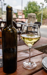 Glass of white wine and bottle of wine on a wooden table in restaurant outdoor terrace
