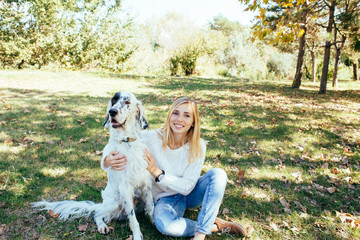 happy young woman in a white sweater and blue jeans hugging a big white dog in the park