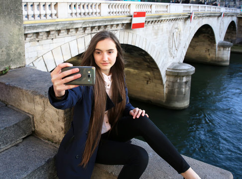 Beautiful young tourist girl making selfie near the bridge in Paris