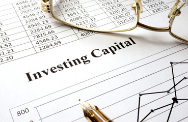 Sign investing capital on a paper and glasses.