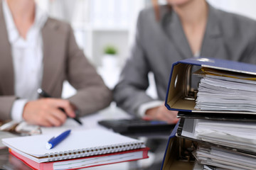 Binders with papers are waiting to be processed with businessman and secretary back in blur....