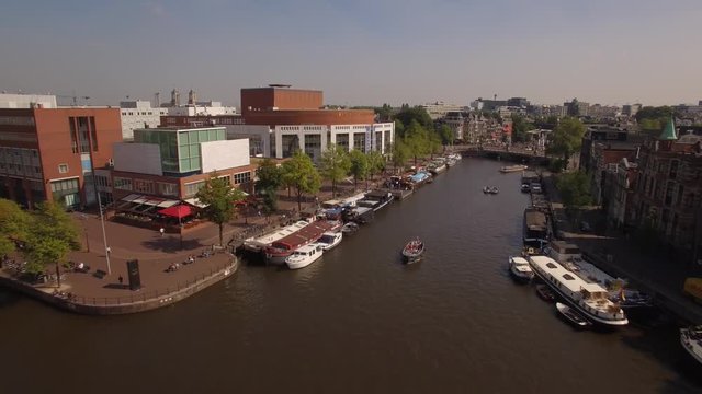 Aerial. Tour boats on water channel in Amsterdam. Camera moves back. 4K