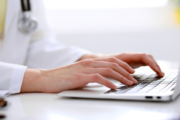 Close-up of female doctor typing laptop sitting at a table in the hospital