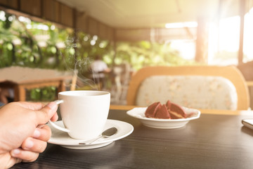 Fototapeta na wymiar Sunrise Monring with hand holding a coffee cup with red cake at coffee shop