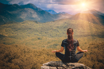 Naklejka na ściany i meble Young woman sits at peak of mountain in lotus pose, doing yoga and feel harmony of body and nature. Relax and meditation on outdoor.