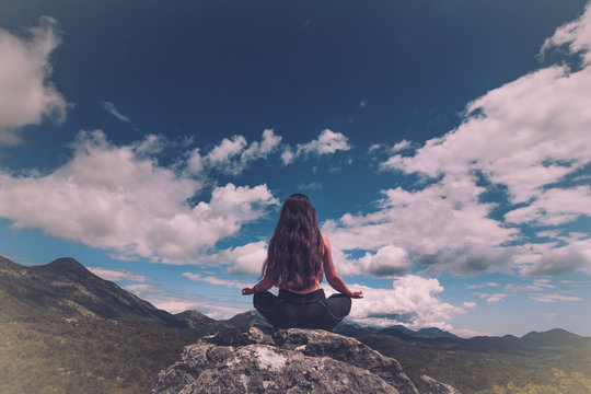 Woman sits at peak of mountain in  lotus pose, doing yoga and feel harmony of body and nature. Relax and meditation on outdoor. 