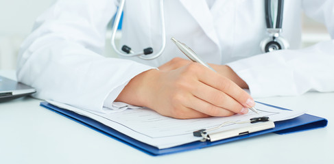 Female doctor is sitting at the table and filling up medical application form. Health care, insurance and help concept.