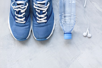 Flat lay sport shoes, bottle of water and earphones on gray conc