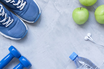 Flat lay sport shoes, dumbbells, earphones, apples, bottle of wa