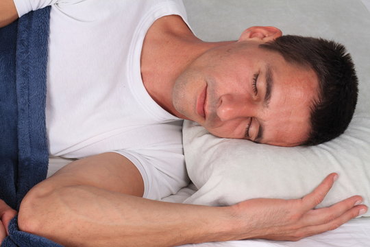 Portrait of young handsome man comfortably sleeping in bed at home