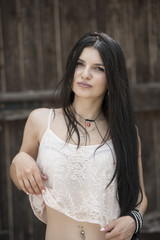 Fototapeta premium Portrait of a woman with a very long straight black wear gauzy crop top against old wooden door