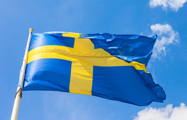 Swedish flag with yellow cross waving in the wind on a blue sky