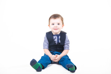 Cute kid in a striped knitted socks, blue jeans and a batch file with a vest sits isolated on a white background