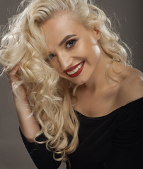 beauty portrait of a positive blond with red lipstick , a black shirt , holding a hand hair