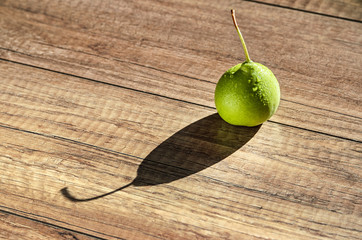 Swadow from pear. Alone juicy green pear with water drops cast a long shadow on wood background 