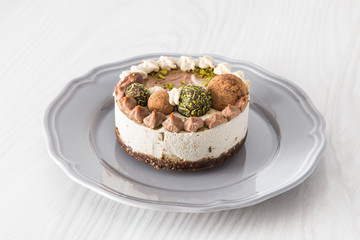 Raw vegan cake with lime, banana and chocolate, decorated with lime zest and chocolate balls on a grey plate on a light background 