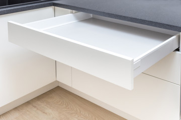 Opened white drawer in a kitchen cabinet with an handleless front, tip to open system 