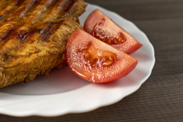 Fototapeta premium grilled chicken breast with tomatoes served on white plate on wooden table