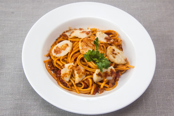 Pasta (spaghetti) with scallops and tomato sauce is on the plate