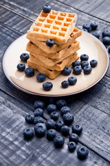 Blueberries and sweet waffles on plate and blue wood